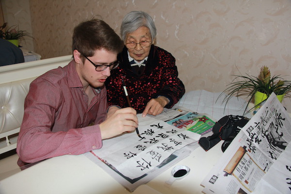 A young man paints calligraphy while an elderly woman directs him.