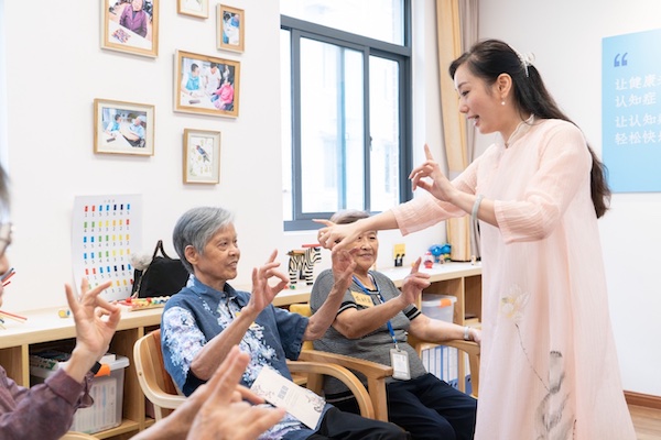 A young woman and a group of elderly people are holding finger shapes.