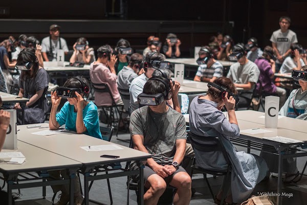 A large group of people sitting at different tables wear VR headsets.
