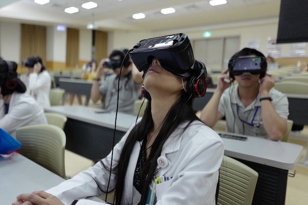 A woman in a lab coat sits, wearing a VR headset.