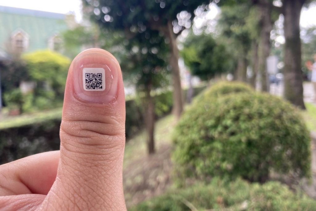 A photo of an Orange Links QR Code sticker on someone's thumb.
