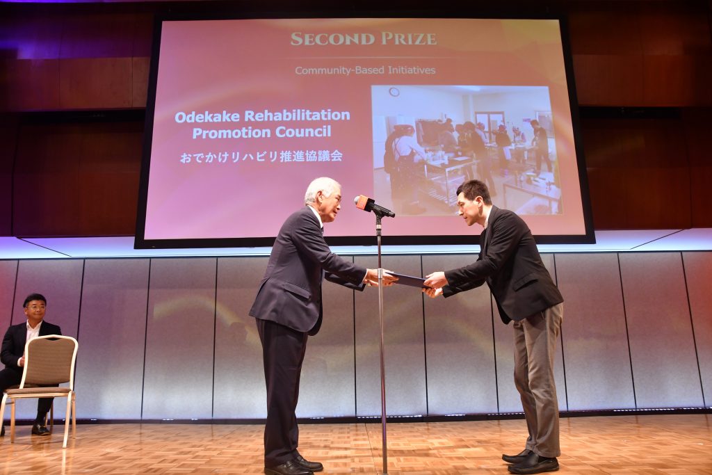 Mr. Teiichi Matsuda, Chair of the Odekake Rehabilitation Promotion Council, receives the Second Prize for Community-Based Initiatives from JCIE's president Akio Okawara